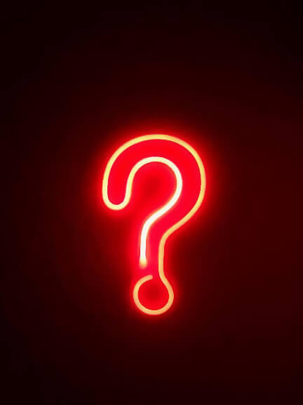red neon sign shaped like a question mark against a dark wall