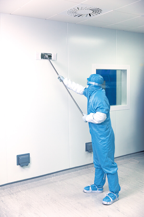 A gowned lab tech sweeping the walls of a facility with a dust mop