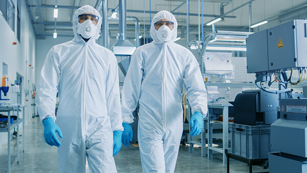 Two gowned and covered engineers walking on the floor of a manufacturing facility side by side