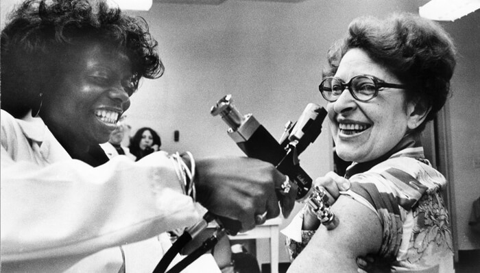 A vintage black and white photo of a nurse administrating a swine flu vaccination with an auto injector