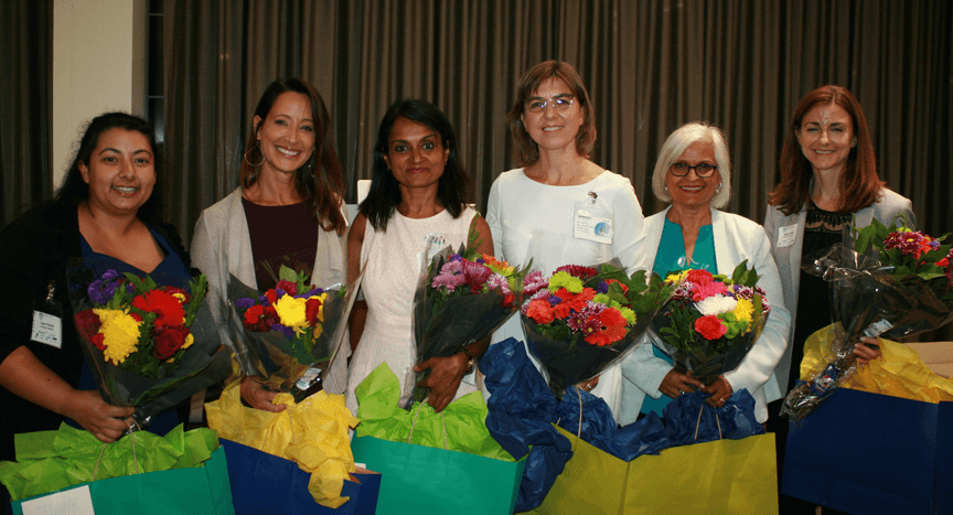 The six panelists all stand together holding flowers from the PDA West Coast Chapter at the event
