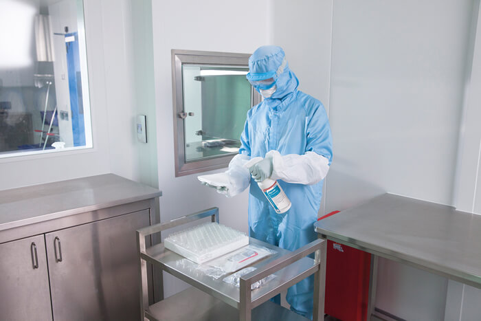 A gowned up scientist spraying down a white cloth with a disinfectant spray