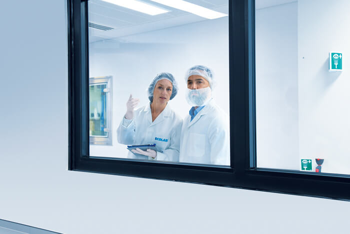 Two gowned scientists at an observation window looking into a facility