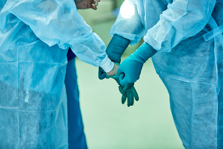 two workers assisting one another in putting on gloves while sterile gowning