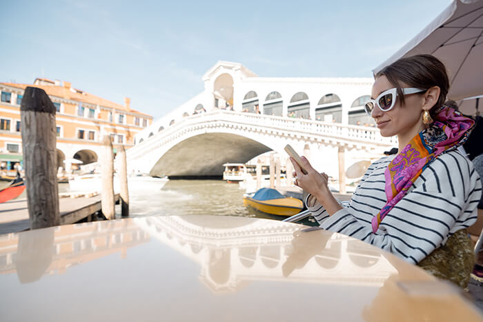 A woman reading on her phone at a cafe overlooking the Grand Canal in Venice, Italy