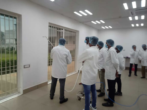 Attendees in labcoats, hairnets, and masks watch a demonstration of surface cleaning